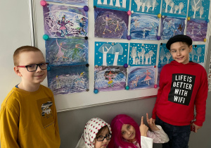 Dwóch uczniów i dwie uczennice na tle prac plastycznych.