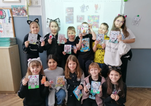 Uczniowie z klasy 2a w kocich przebraniach prezentujący wykonane prace plastyczne