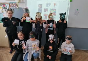 Uczniowie z klasy 2a w kocich przebraniach prezentujący wykonane prace plastyczne