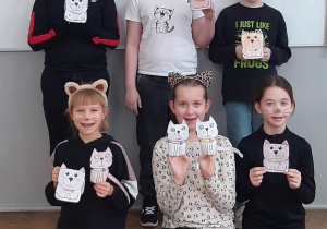 Uczniowie z klasy 3b w kocich przebraniach prezentujący wykonane prace plastyczne