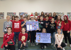 Grupa uczniów stojąca na korytarzu prezentuje dwa plakaty Christmas Jumper Day.