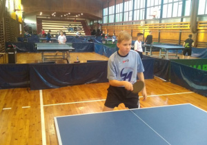 Uczeń w niebieskiej koszulce odbijający piłkę w czasie meczu w tenisa.