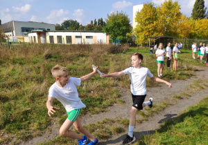 Dwóch chłopców w sportowych strojach podczas biegu przekazują sobie pałeczkę sztafetową.