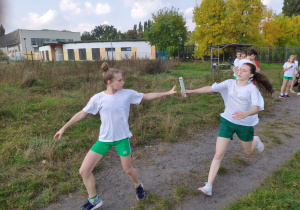 Dwie dziewczynki w sportowych strojach przekazują sobie pałeczkę sztafetową.