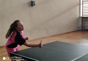 Uczennica w rózowej koszulce podczas rozgrywania meczu w tenisa stołowego.
