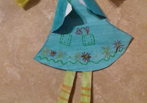 Wycinanka - postać dziewczynki z jasnymi włosami w niebieskiej sukience i niebieskich trzewikach.