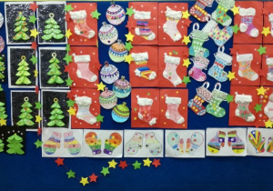 Galeria prac plastycznych związanych ze Świętami Bożego Narodzenia: kolorowe choinki, bombki, rękawiczki, gwiazdki oraz skarpety przeznaczone na prezenty. Wszystkie prace zostały wyeksponowane na tablicy.