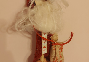 Kukiełka Mikołaja, wykonana z drewnianej łyżki. Mikołaj ma tradycyjny czerwono-biały strój wykonany z materiału i włóczki. Czapka ozdobiona jest białą gwiazdką. Mikołaj trzyma w rękach duży worek z prezentami