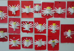 Galeria prac uczniów: biały orzeł (tułów z rolki po papierze owiniętej białym papierem/bibułą, skrzydła oraz ogon wycięte z białego papieru; korona, dziób, szpony wycięte z żółtego papieru) przyklejony na czerwonym kartonie wyciętym na kształt godła