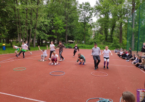 Grupa uczniów zajmująca miejsce w kołach hula-hop podczas zabawy "Wiewiórki do dziupli".