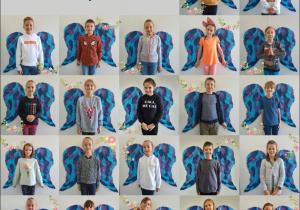 Zdjęcie przedstawia dzieci z klasy 3a stojące na tle dużych niebieskich skrzydeł