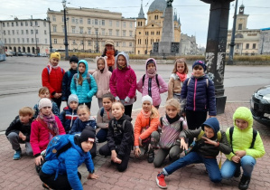 Uczniowie klasy 3a stoją w grupie na Placu Wolności. Na drugim planie widoczny jest Pomnik Tadeusza Kościuszki, Kościół Zesłania Ducha Świętego oraz Archiwum Państwowe.