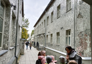 Dzieci wchodzą parami do „Pasażu Róży”. Ściany budynków są szczelnie pokryte kawałkami drobnych, nieregularnie pociętych luster.