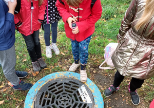 Uczestnicy wycieczki obserwują rzekę Łódkę przepływającą pod Parkiem Staromiejskim przez właz kanalizacyjny tzw. „Oko Śledzia”.