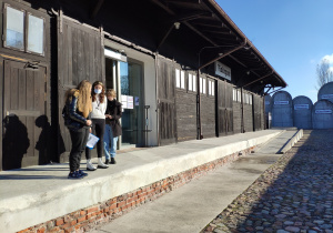 Dwie uczennice i pracownik muzeum stoją na rampie przeładunkowej przy magazynie na Stacji Radegast.