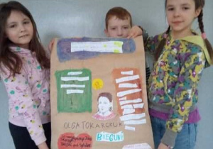 Troje uczniów klasy 3b trzyma wykonany przez siebie plakat przedstawiający postać Olgi Tokarczuk