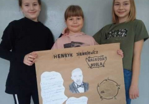 Trzy uczennice klasy 3b trzymają wykonany przez siebie plakat przedstawiający postać Henryka Sienkiewicza.
