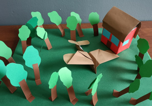 Makieta jednej ze scen z lektury – Lądowanie samolotu w ogrodzie u cioci Eli. Widoczne są drzewa z papieru na zielonym tle, dom oraz brązowy samolot z papieru wykonany techniką Origami.