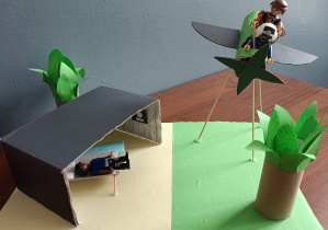 Makieta jednej ze scen z lektury – Lot samolotu do cioci Eli. Na planszy z papieru stoi dom, obok niego drzewa. Obok widoczny jest nadlatujący samolot z papieru umieszczony na długich patyczkach. W samolocie siedzi pilot i Waluś. Obie postaci wykonane są z klocków Lego.