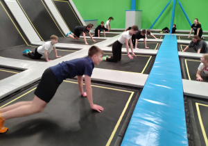Uczniowie wykonują ćwiczenia na trampolinach. Po wyskoku przechodzą do leżenia