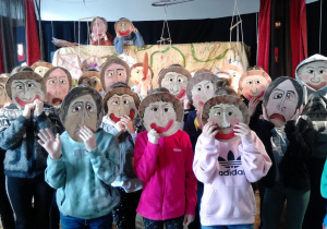 Zdjęcie przedstawia uczniów klasy 3a podczas warsztatów teatralnych zasłaniających twarze maskami teatralnymi.