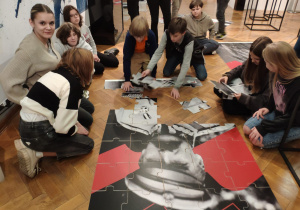 Grupa uczniów układająca puzzle z postacią Józefa Piłsudskiego.