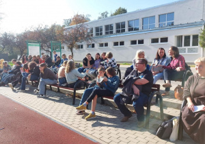 Uczniowie obserwujacy mecz koszykówki na boisku szkolnym.