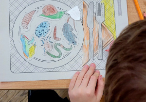 Uczeń prezentuje swoją pracę plastyczną - narysowany talerz ze smakołykami dla jeża