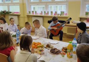 Zdjęcie przedstawia uczniów klasy 2b przy świątecznym stole, słuchających kolegi grającego na gitarze