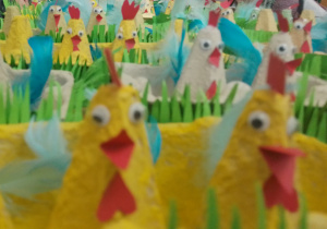 Zdjęcie przedstawia koguty wielkanocne wykonane z wytłaczanek po jajkach, ozdobione papierem, kolorowymi piórkami. Praca zrobiona przez uczniów klasy 1a.