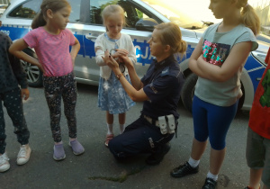 Policjantka pokazuje dzieciom, jak zakłada się kajdanki. Prezentuje to na przykładzie dziewczynki.