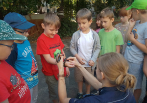 Policjantka pokazuje dzieciom, jak zakłada się kajdanki. Prezentuje to na przykładzie chłopca.