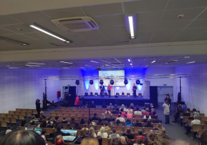 Uczniowie w auli słuchają powitania organizatorów