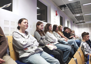 Uczniowie w auli słuchają powitania organizatorów