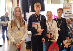 Czworo zawodników na zdjęciach udekorowanych pamiątkowymi medalami i szachowymi gadżetami.