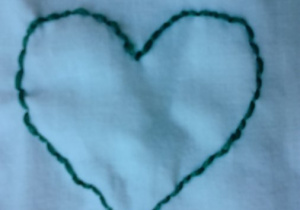 Zielone serce wyszyte ściegiem prostym na białej serwetce.