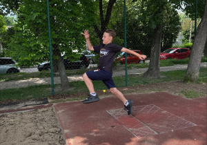Zawodnik SP71 w granatowych spodenkach i czarnej koszulce podczas próby skoku w dal.