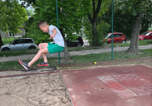 awodnik w zielonych spodenkach i białej koszulce na chwilę przed lądowaniem w skoku w dal.