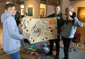 Trzech chłopców prezentuje plakat wykonany na szarym papierze o tematyce związanej z ochroną planety Ziemi.